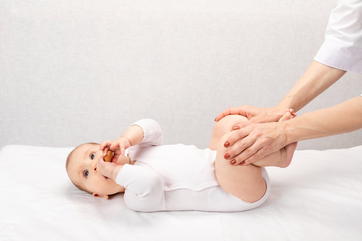 Hände eines Behandlers führen eine körperliche Untersuchung an einem Baby in weißer Kleidung durch